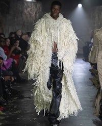 a model walks down the runway in a fur coat and leather pants