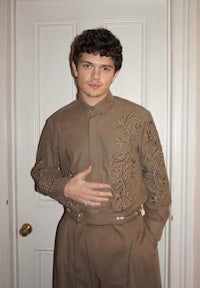 a young man in a brown suit posing in front of a door