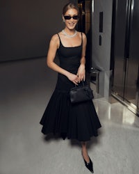 a woman wearing a black dress and sunglasses is standing in an elevator