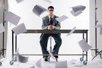 a businessman sitting at a table with papers flying around him